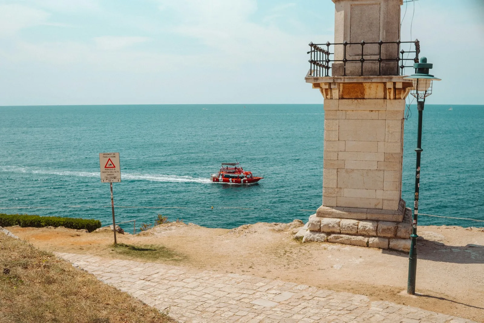 A red tour boat passing the Punta Corrente lighthouse off Rovinj