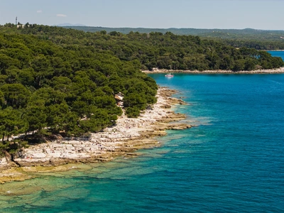 Rotsachtige kust met een passerende boot en het silhouet van Rovinj