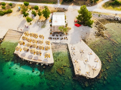 Slamniki in ležalniki na kamnitih ploščadih ob plažnem baru.