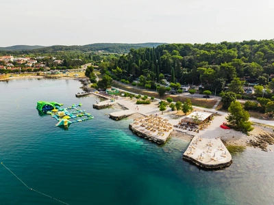 Kamnite terase in barski lokal ob plaži sredi borovega gozda severno od starega dela mesta.